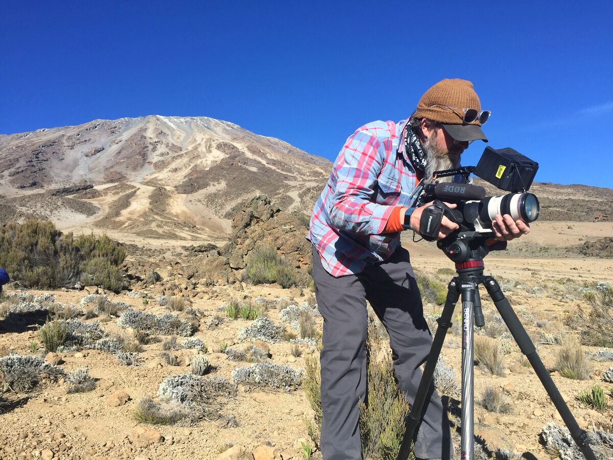 Mike Murphy filming with a cinema camera on a tripod on the slopes of Mount Kilimanjaro